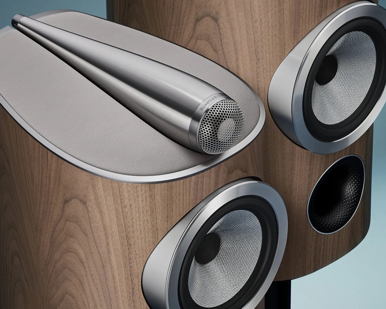 Wood-finished Bowers & Wilkins speaker with silver cone drivers and a metallic tweeter on a gray leather pad.