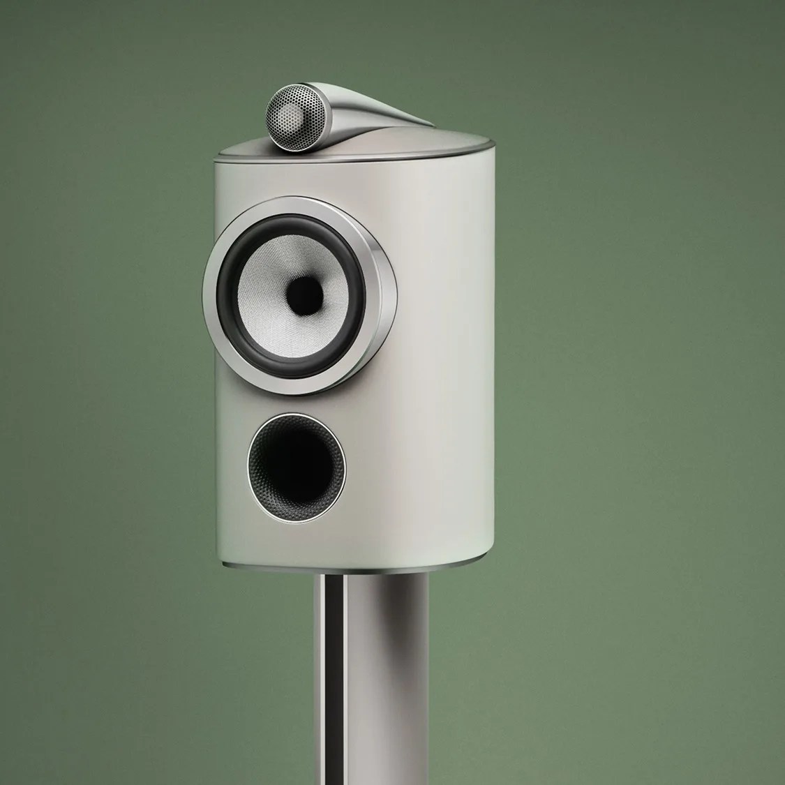 Silver modern speaker with a cylindrical shape and a small tweeter on top against a green background.