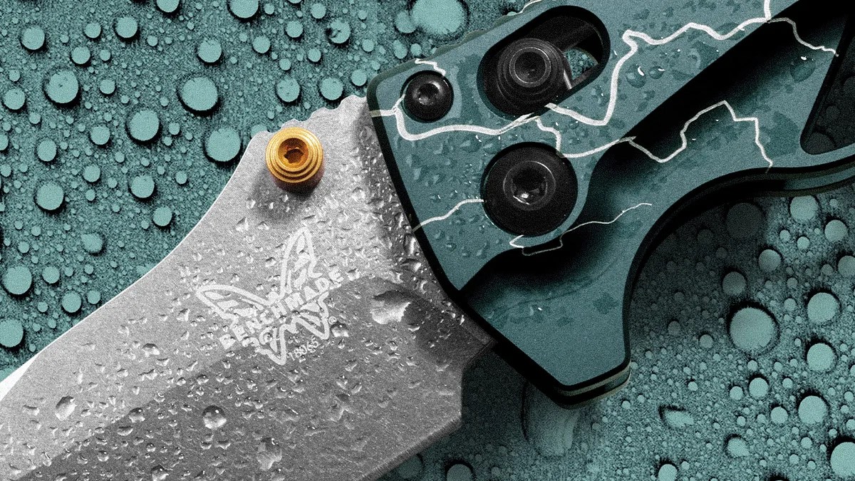 Close-up of a Benchmade folding knife blade and handle with water droplets on a textured surface.