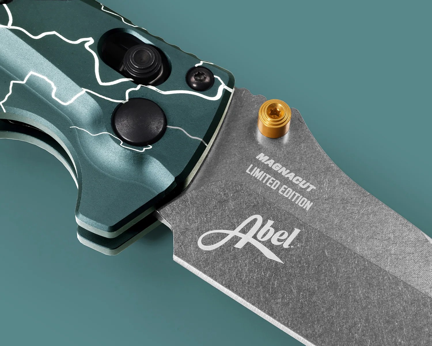 Close-up of a folding knife with a green handle featuring white lightning patterns and a stonewashed blade engraved with "MAGNACUT LIMITED EDITION Abel.