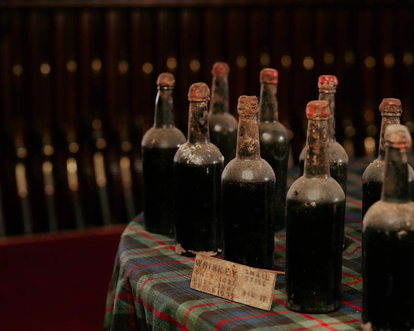 Old dusty dark glass bottles with red wax seals on a plaid cloth-covered table.