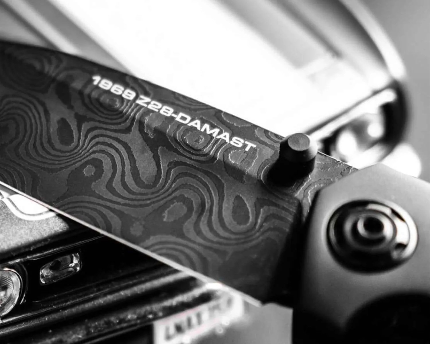 Close-up of a black Damascus patterned knife blade with "1969 Z28-DAMAST" text near the handle.
