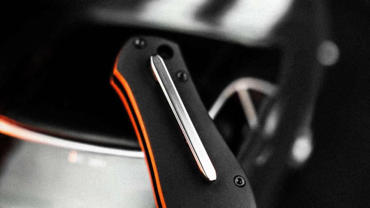 Close-up of a black folding knife handle with orange accents and a silver pocket clip.