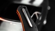 Close-up of a black folding knife handle with orange accents and a silver pocket clip.