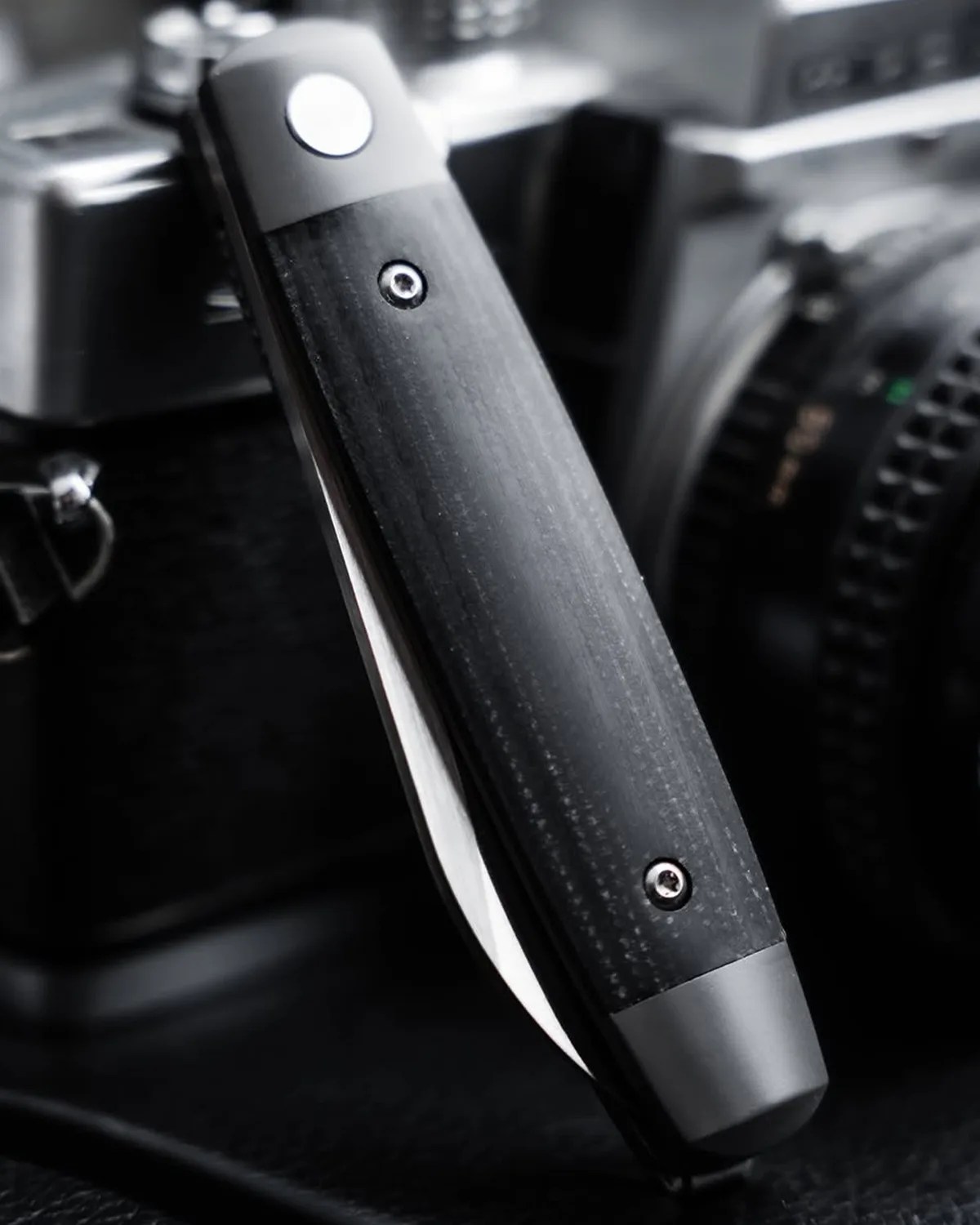 Black folding knife with a textured handle and visible screws, partially open on a dark surface.