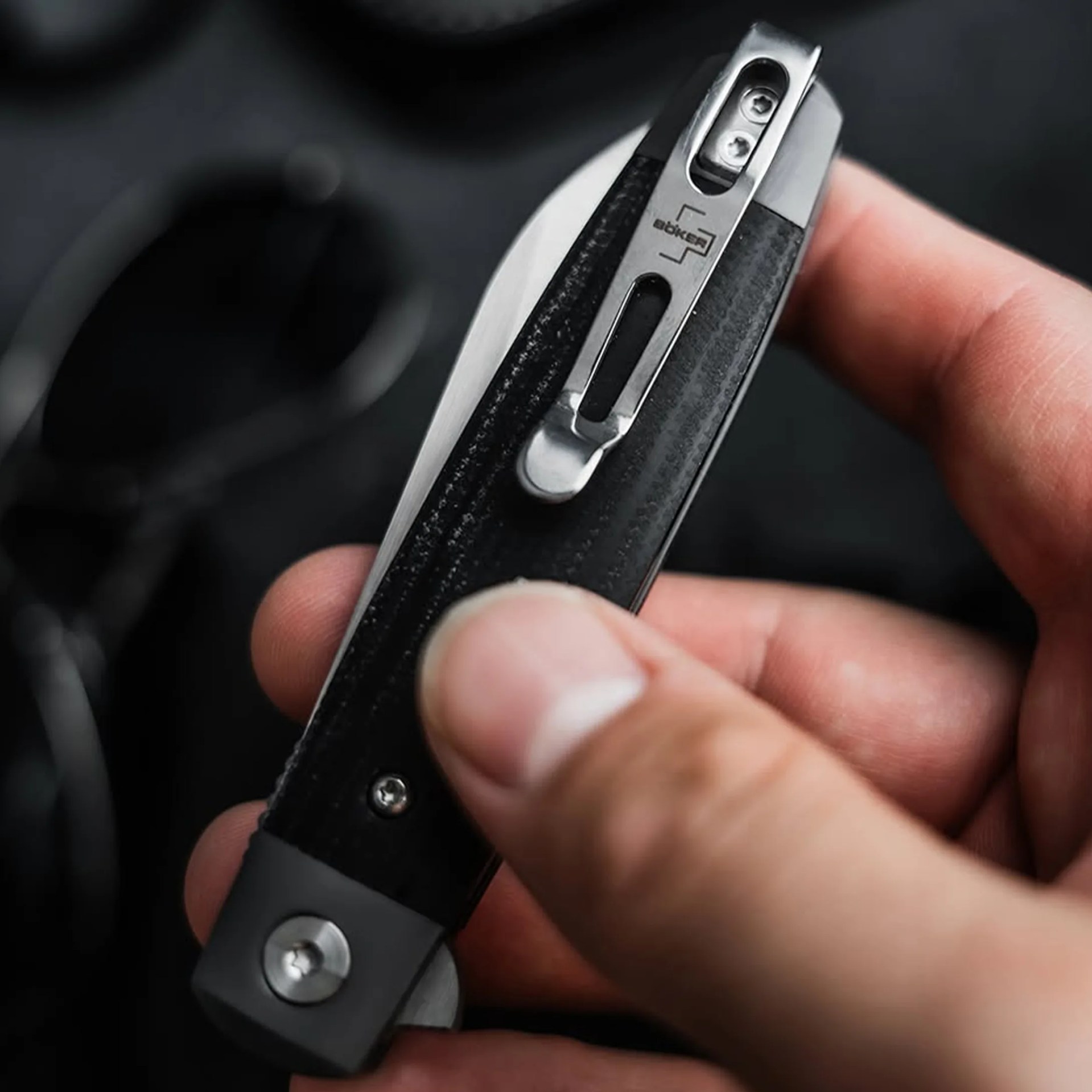 Hand holding a black folding knife with a metal clip engraved with "Böker.