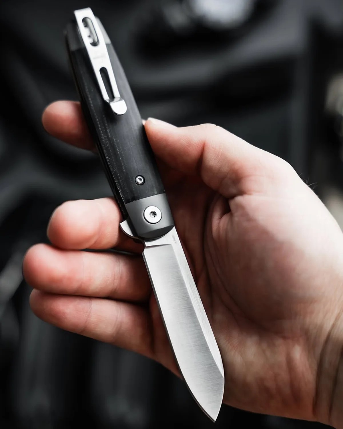 Hand holding a folding knife with a black handle and a partially open stainless steel blade.