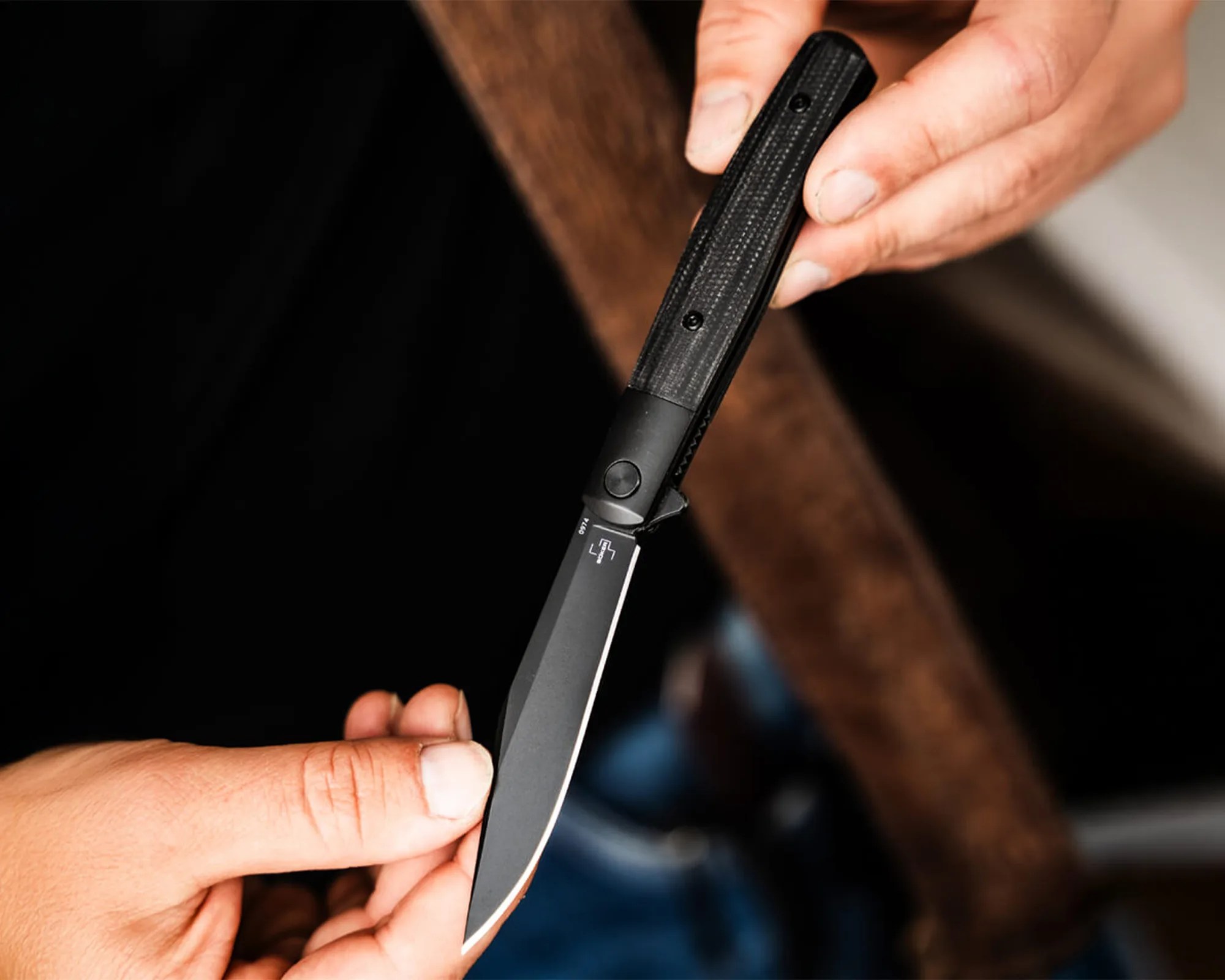 Hand holding a black straight razor with a textured handle and a sharp blade.