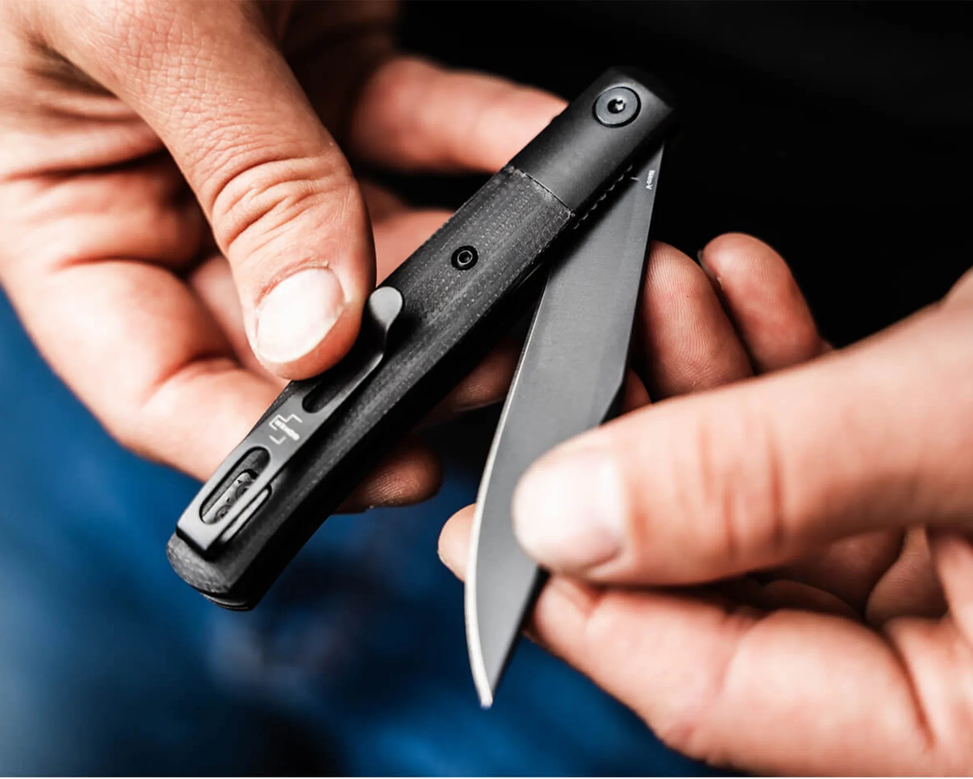 Person holding a black folding knife with a partially open blade and textured handle.