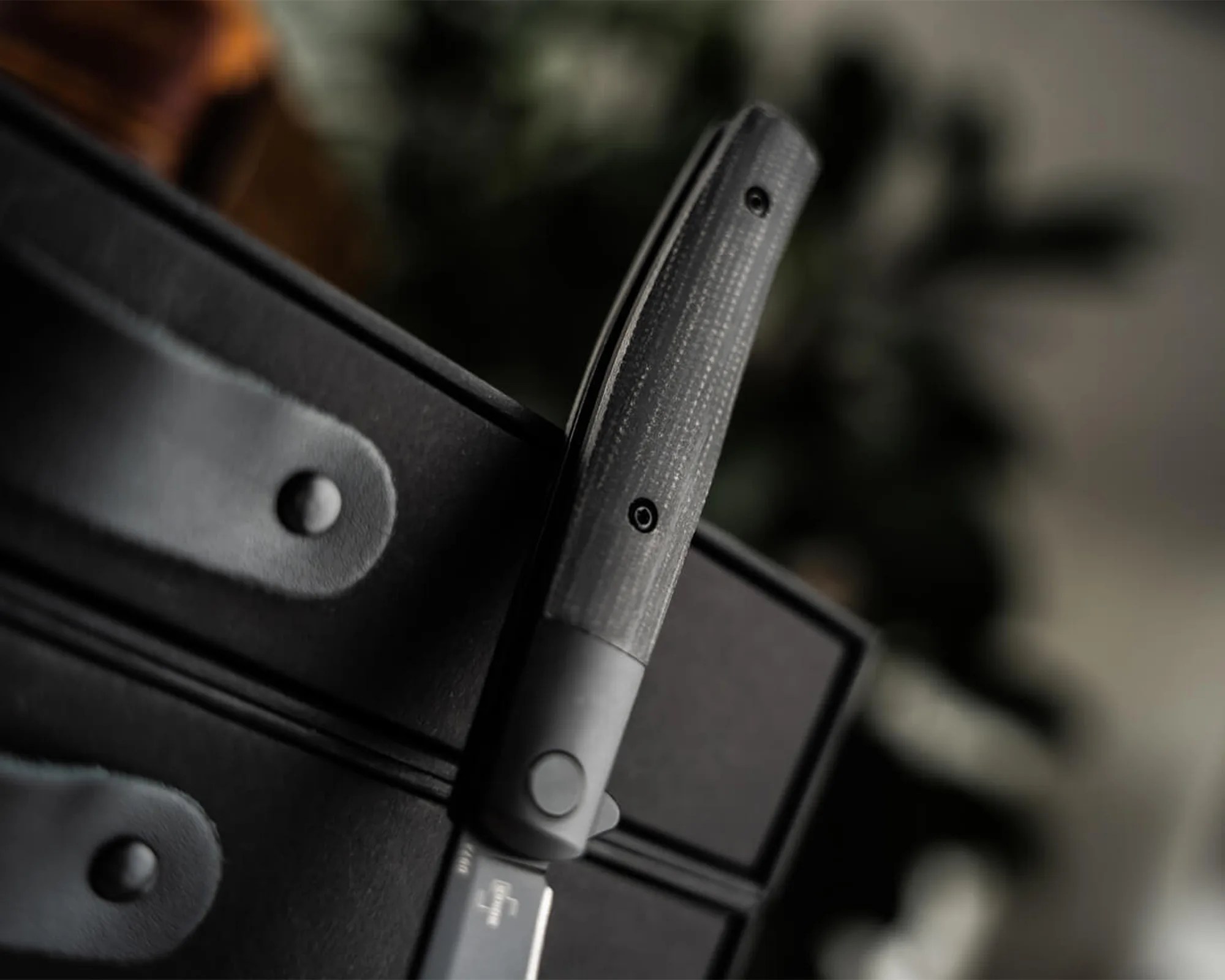 Close-up of a black textured handle attached to a black fabric surface with a button and rivet.