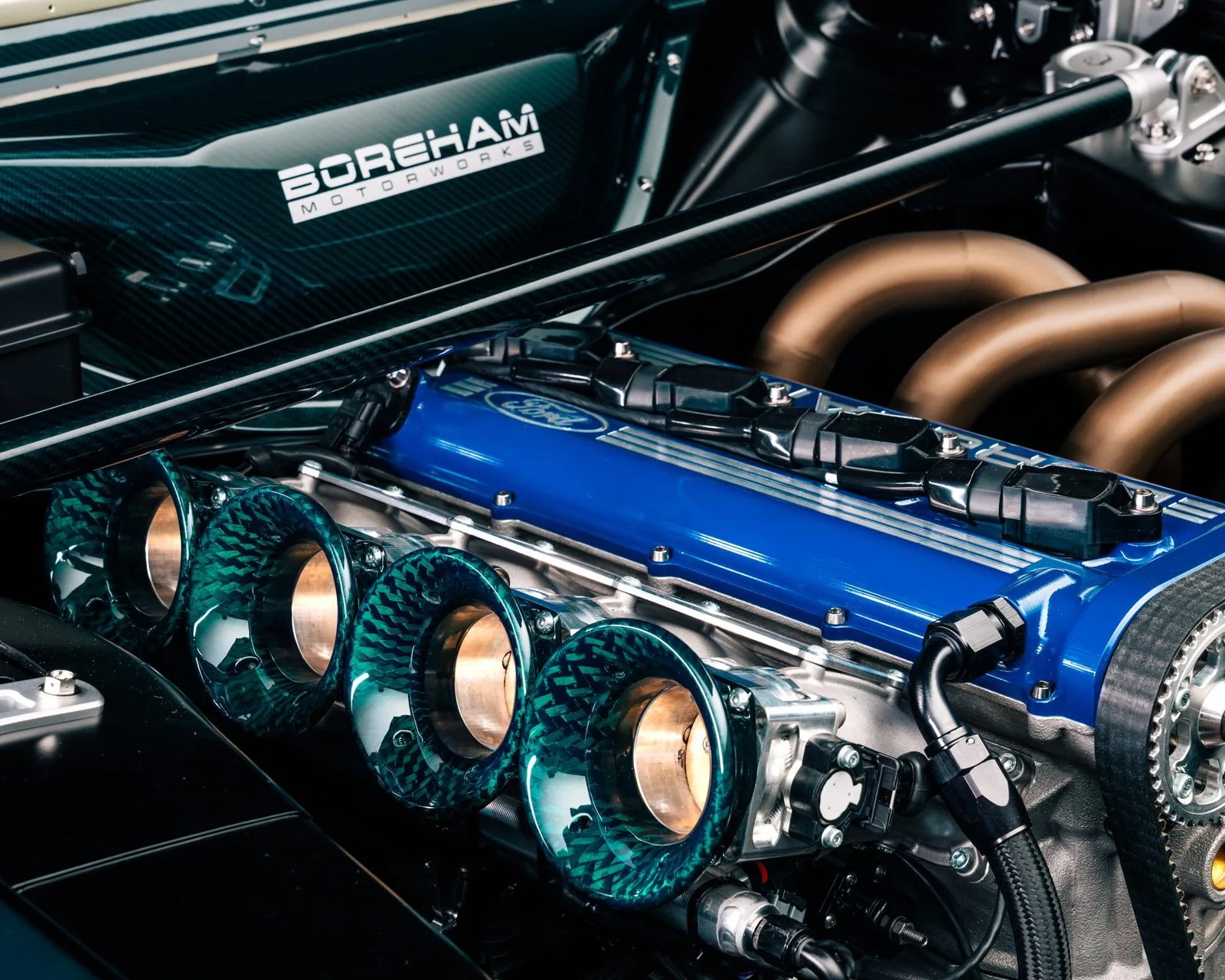 Close-up of a blue Ford engine with carbon fiber intake trumpets and Boreham Motorworks branding on a carbon fiber panel.
