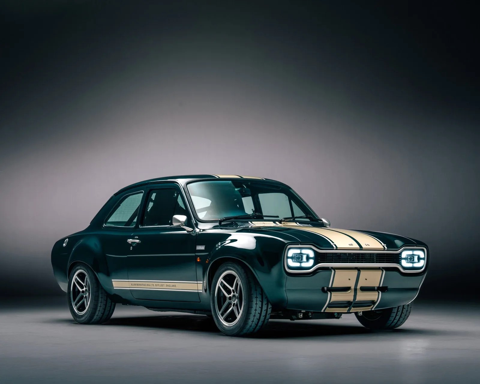 Dark green classic car with beige racing stripes and modern square LED headlights in a studio setting.