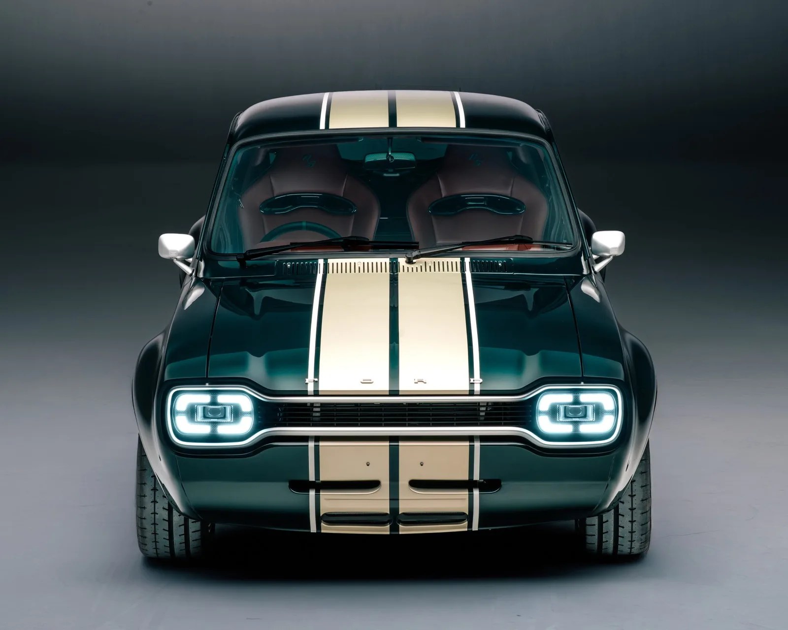 Dark green vintage Ford car with cream racing stripes and illuminated rectangular headlights, front view.