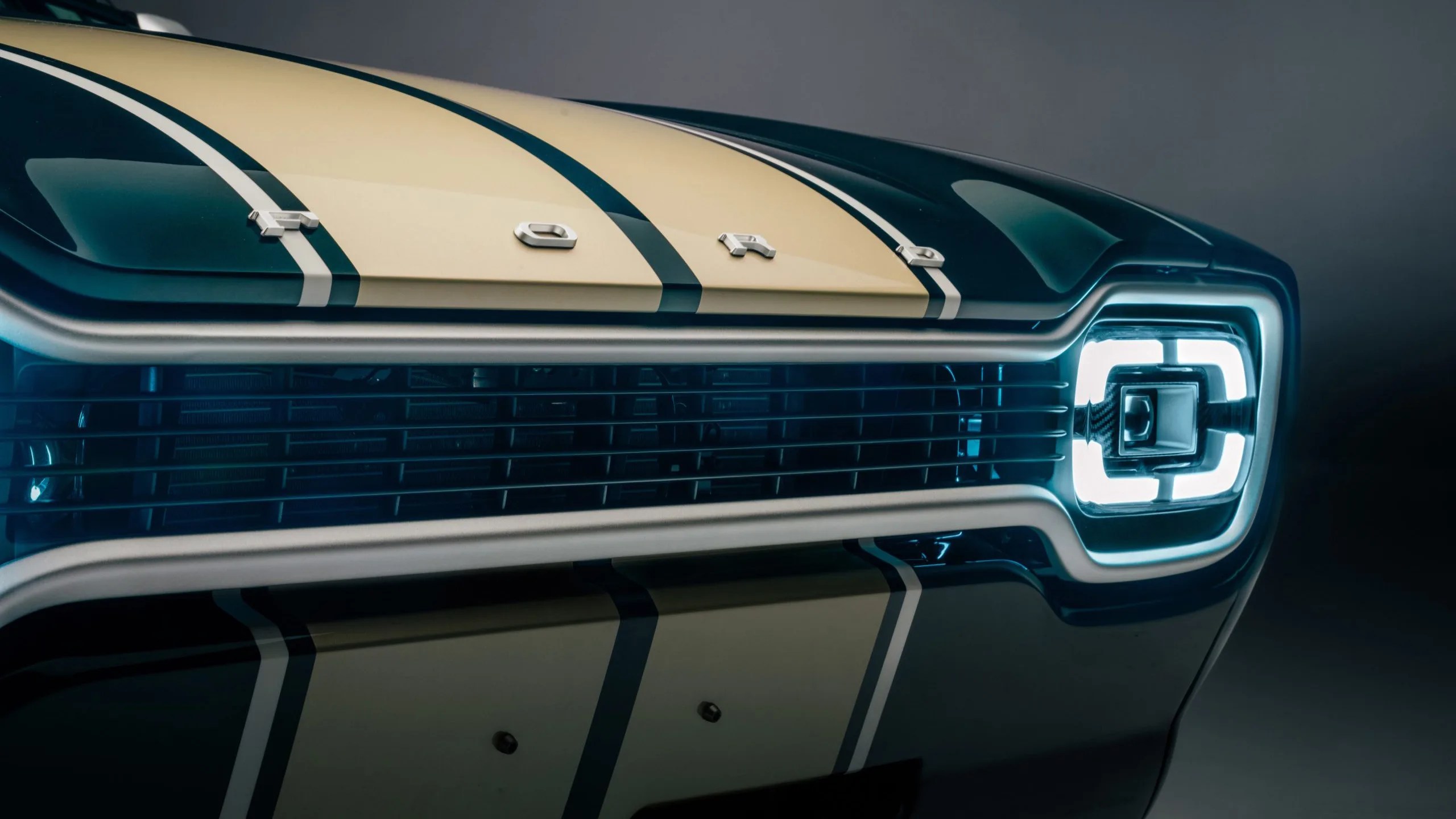 Close-up of a dark green Ford car front with cream racing stripes and illuminated square LED headlight.