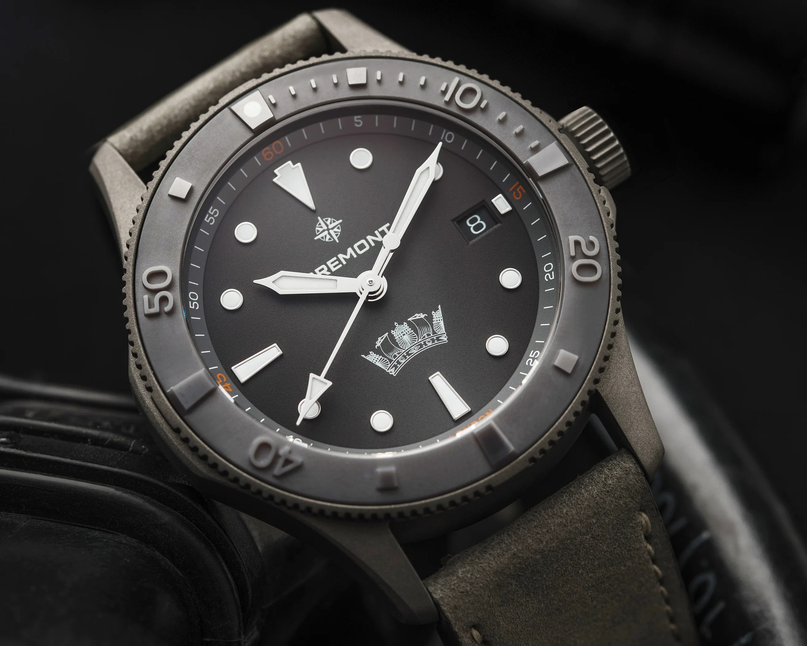 Close-up of a Bremont wristwatch with a matte gray bezel, black dial, white markers, and gray leather strap.