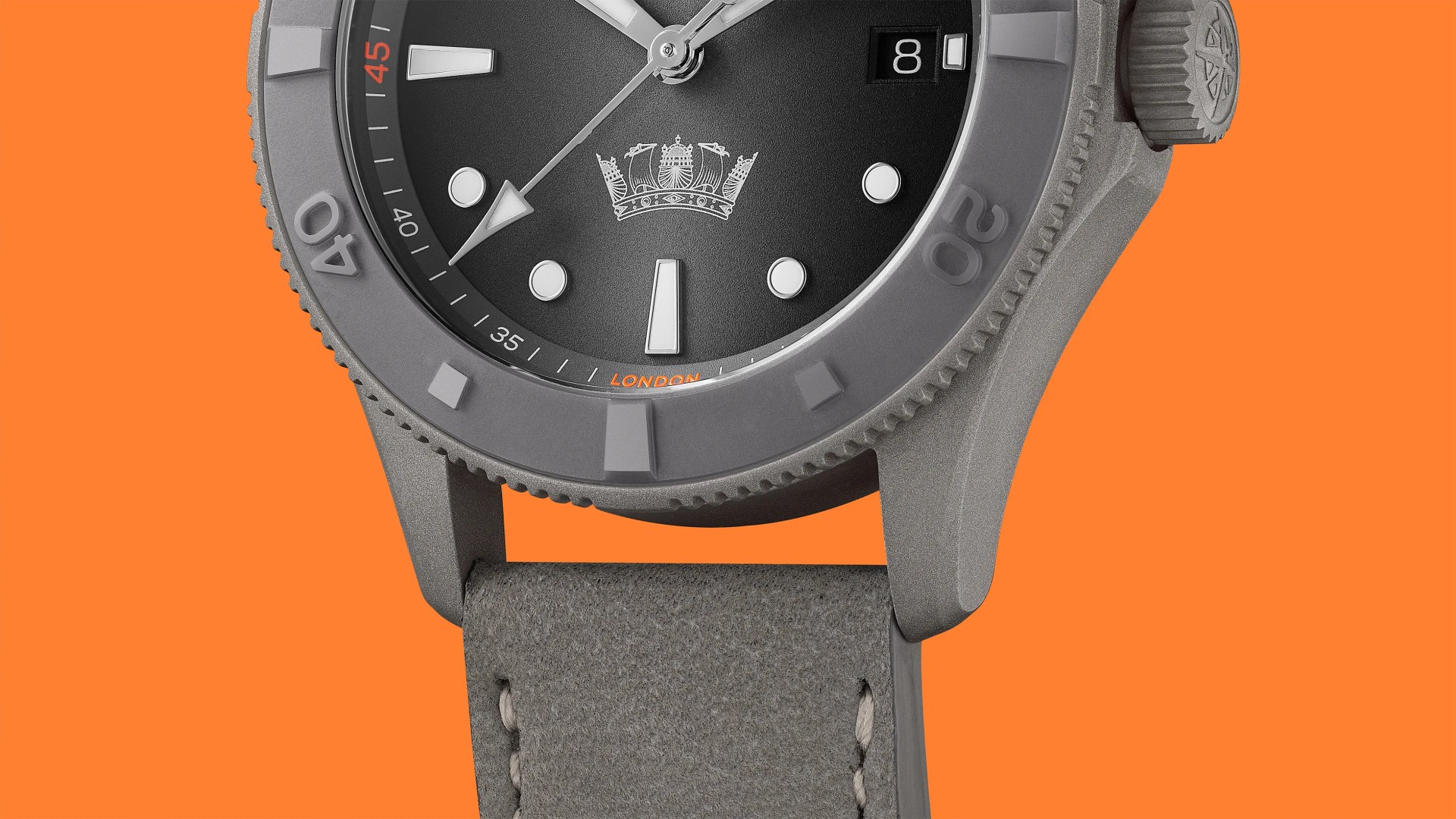 Close-up of a gray wristwatch with a black dial, white markers, a crown emblem, date window, and gray leather strap on an orange background.