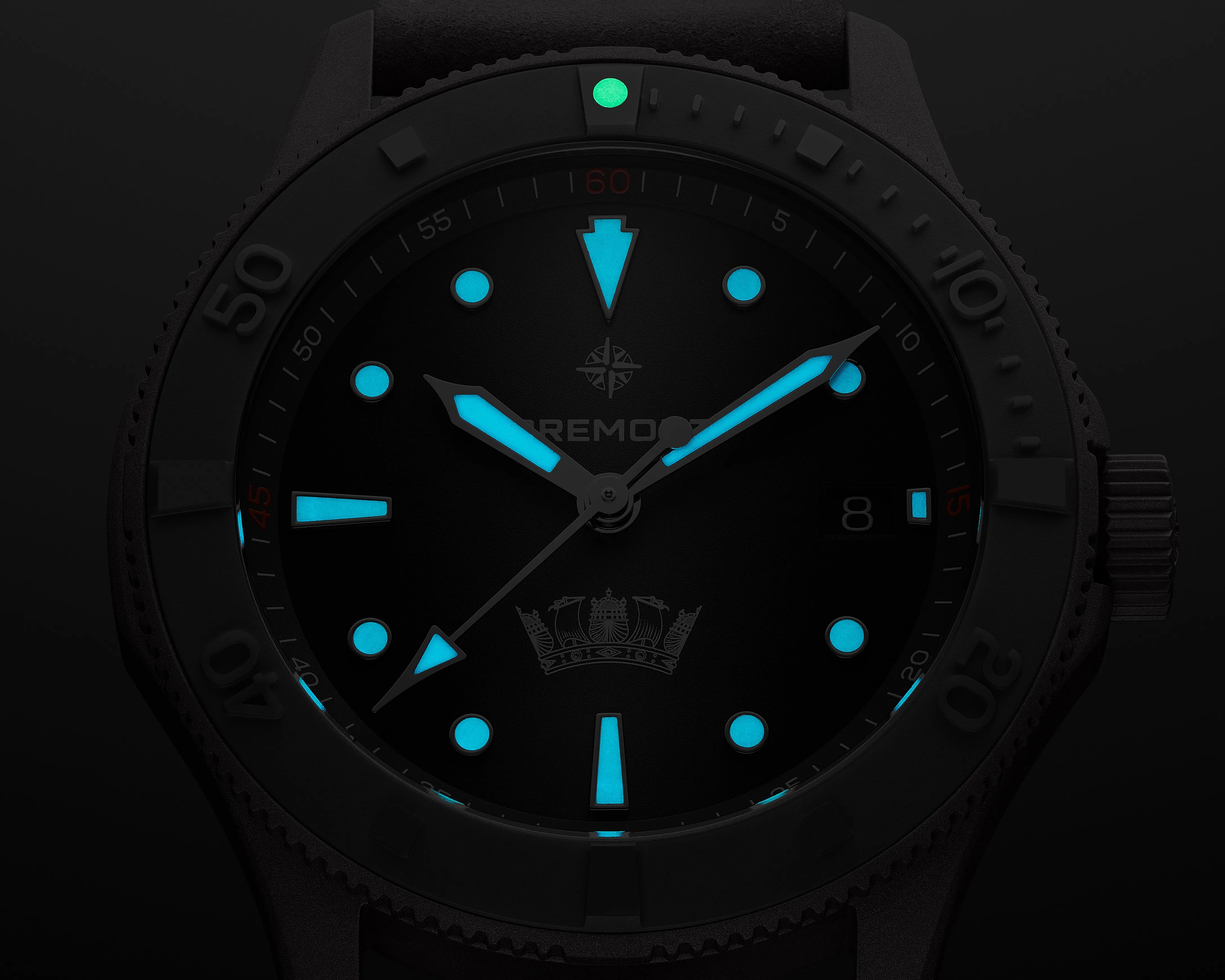 Close-up of a black watch face with blue luminescent hour markers and hands, and a green luminescent dot at the 12 o'clock bezel position.