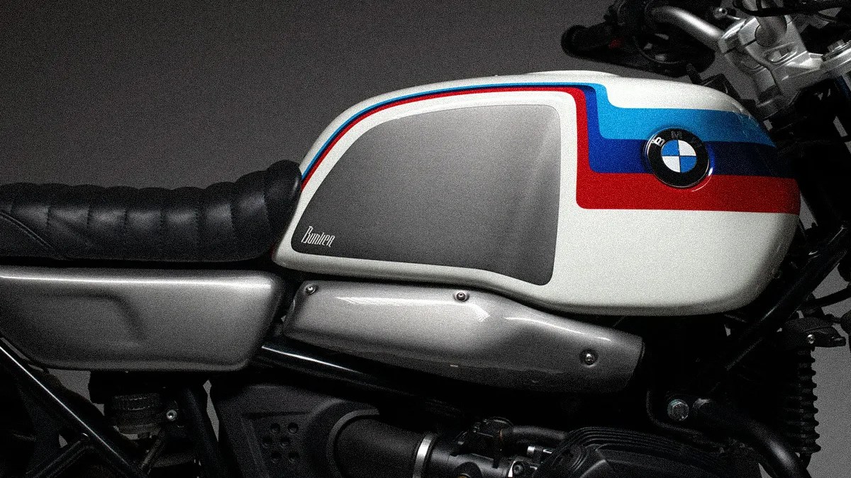 White BMW motorcycle fuel tank with blue and red stripes and black leather seat.