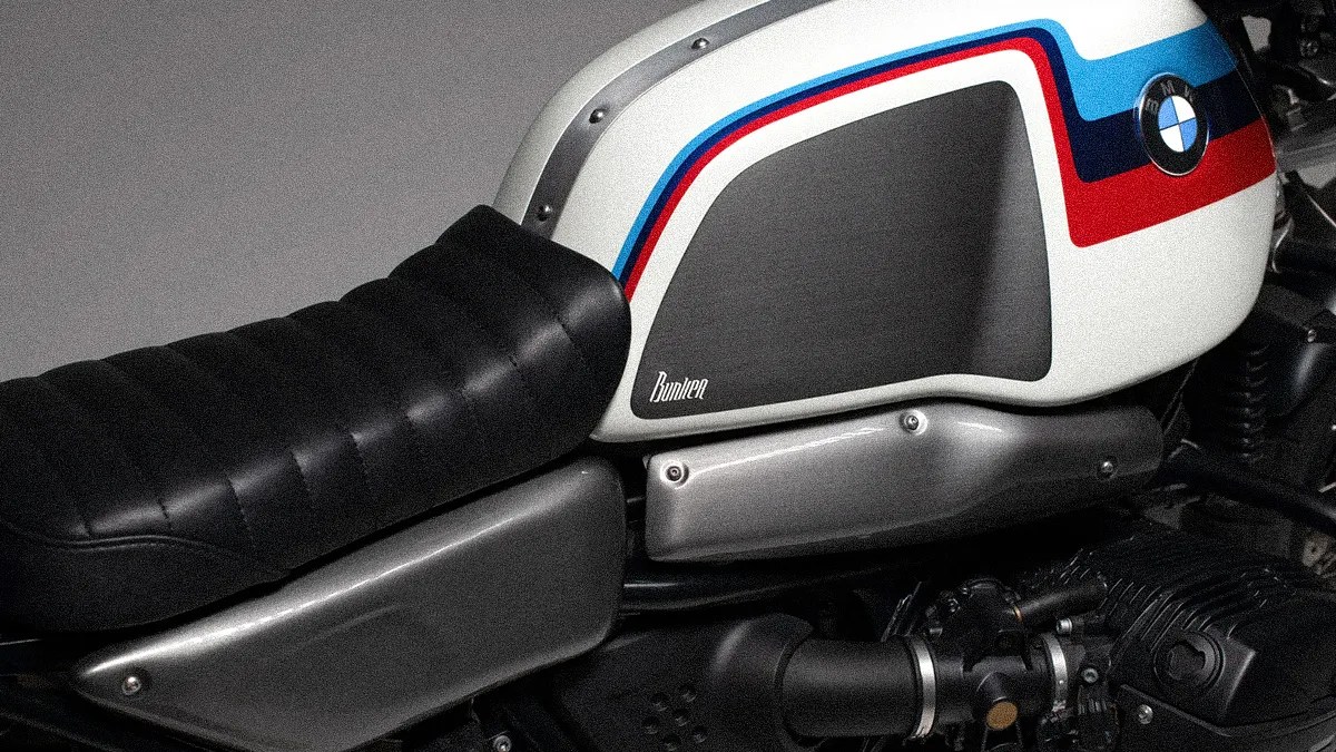 Close-up of a BMW motorcycle fuel tank with red, blue, and light blue stripes and a black leather seat.