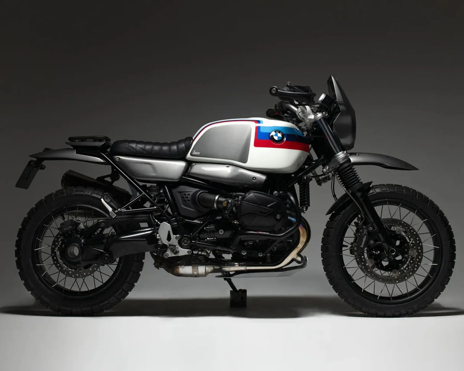 White and silver BMW motorcycle with black frame, knobby tires, and red and blue stripes on the fuel tank.