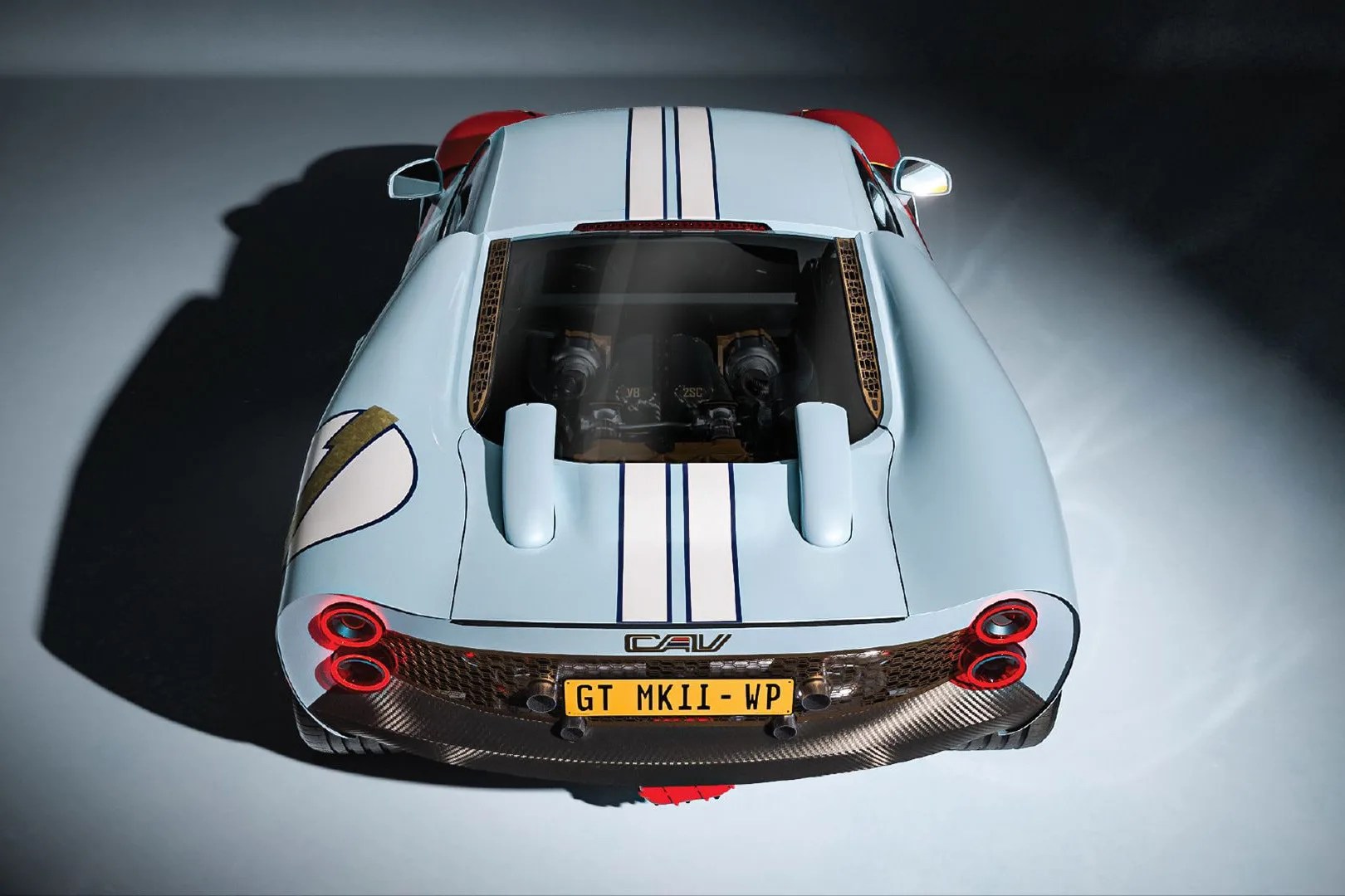 Light blue sports car with white racing stripes and visible engine through rear window.