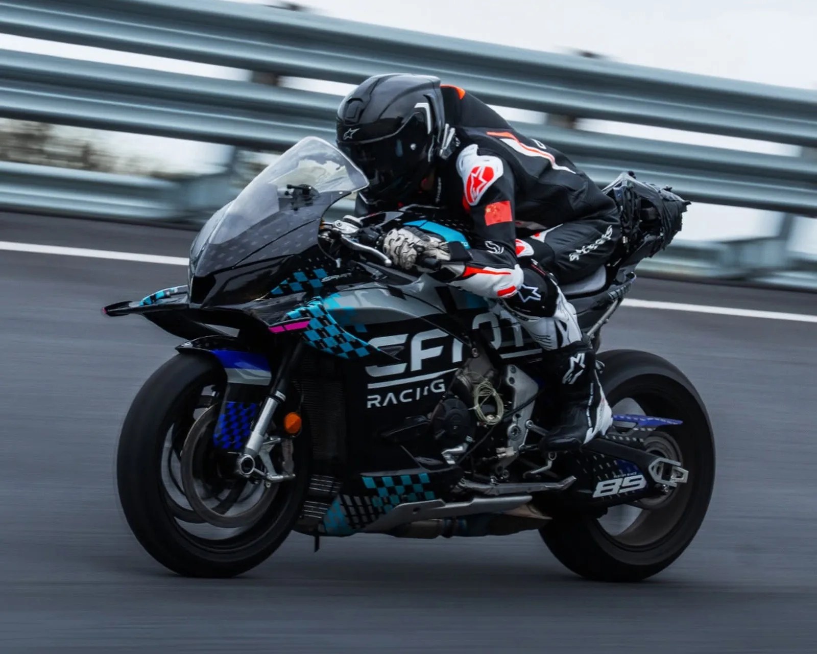 Black and blue racing motorcycle with rider in black and white gear on a racetrack.