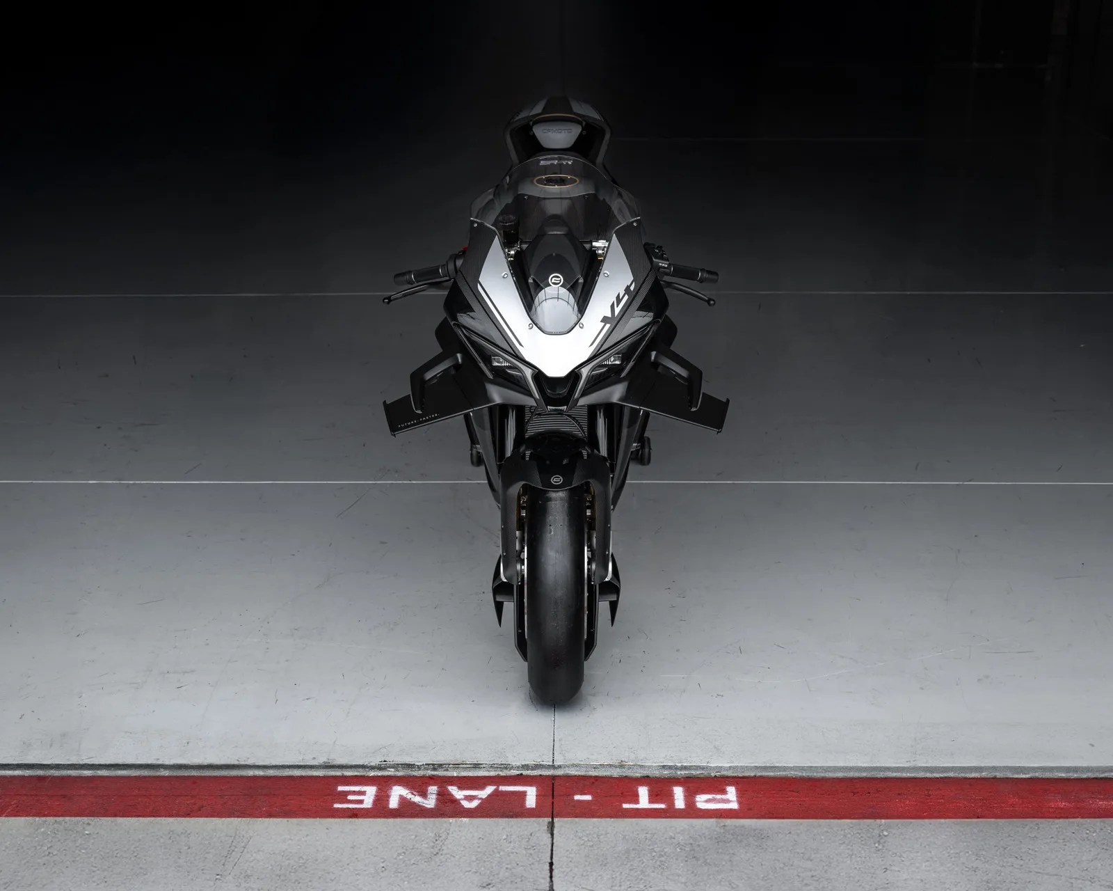 Front view of a black sport motorcycle positioned behind a red "PIT LANE" marking on a concrete floor.