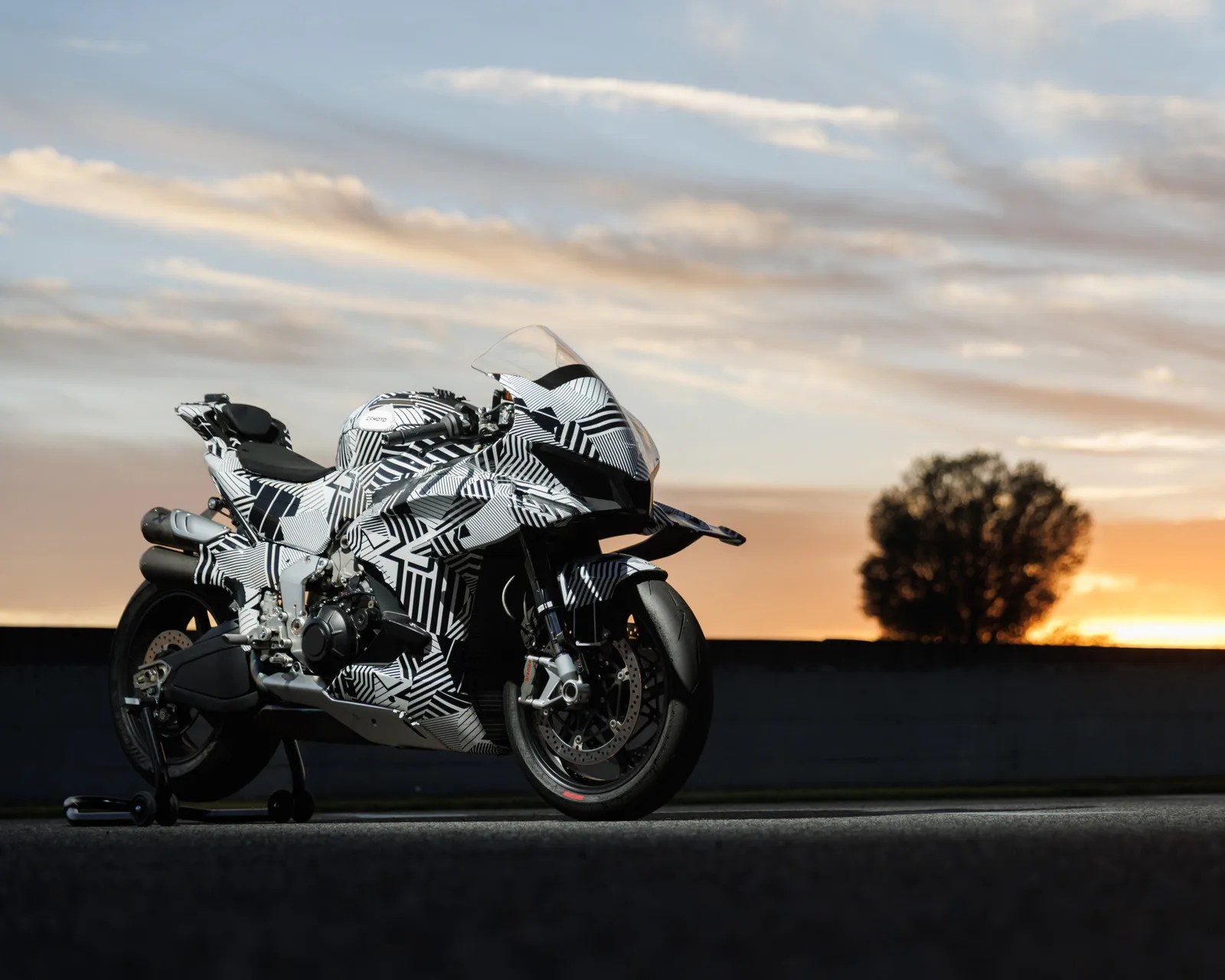 Sport motorcycle with black and white geometric camouflage pattern parked on a stand at sunset.