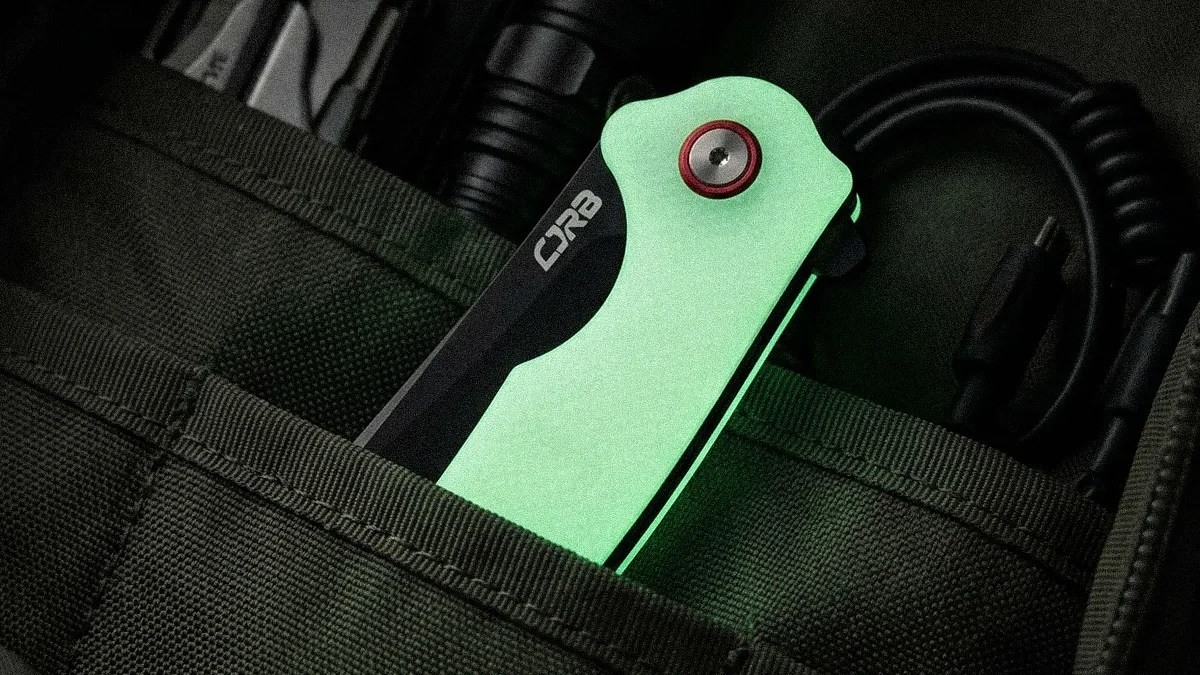 Folded green CRB pocket knife with red pivot screw in a dark green fabric pouch.