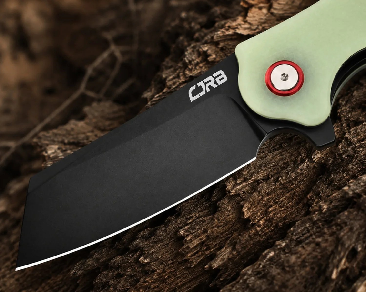 Black blade knife with a light green handle and red pivot screw resting on rough bark.
