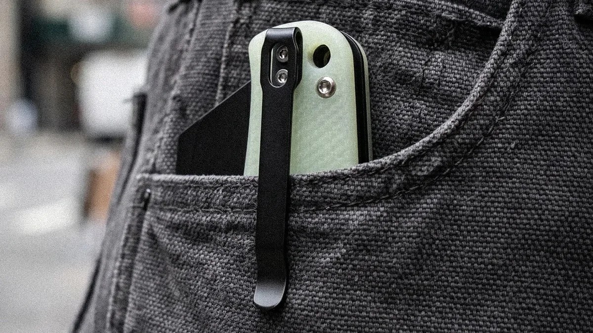 Pocket knife with light green textured handle and black metal clip in a dark gray fabric pocket.