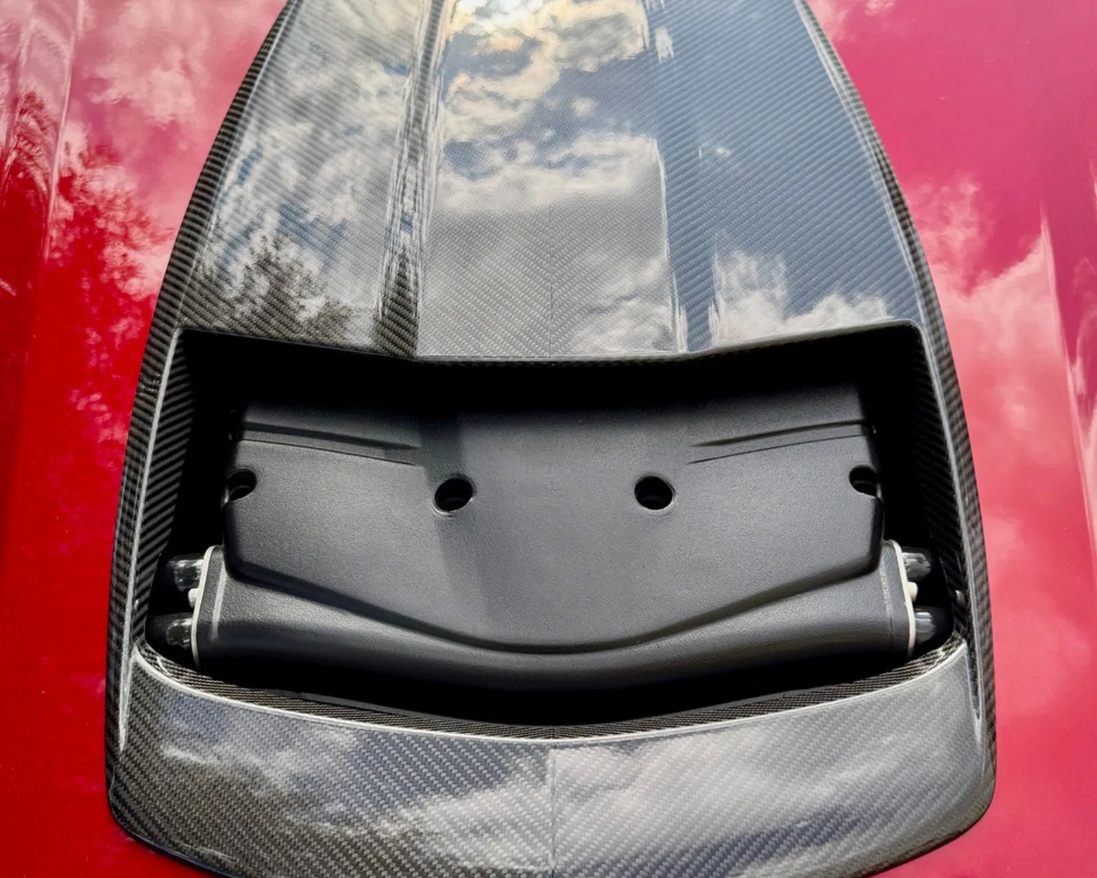 Close-up of a carbon fiber car hood scoop with a black plastic vent insert on a red car.