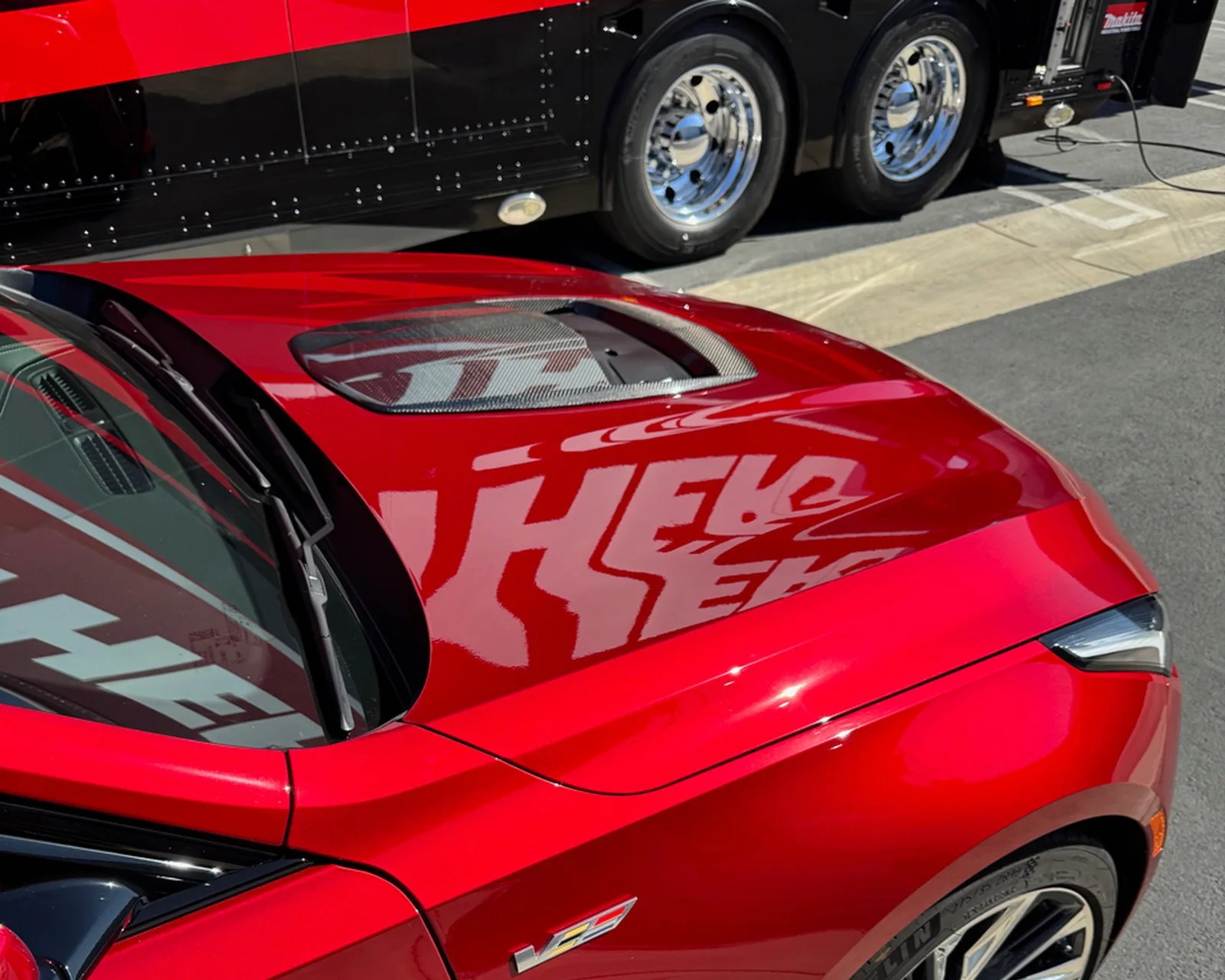 Red car hood with a carbon fiber vent and a V8 badge near the front wheel.