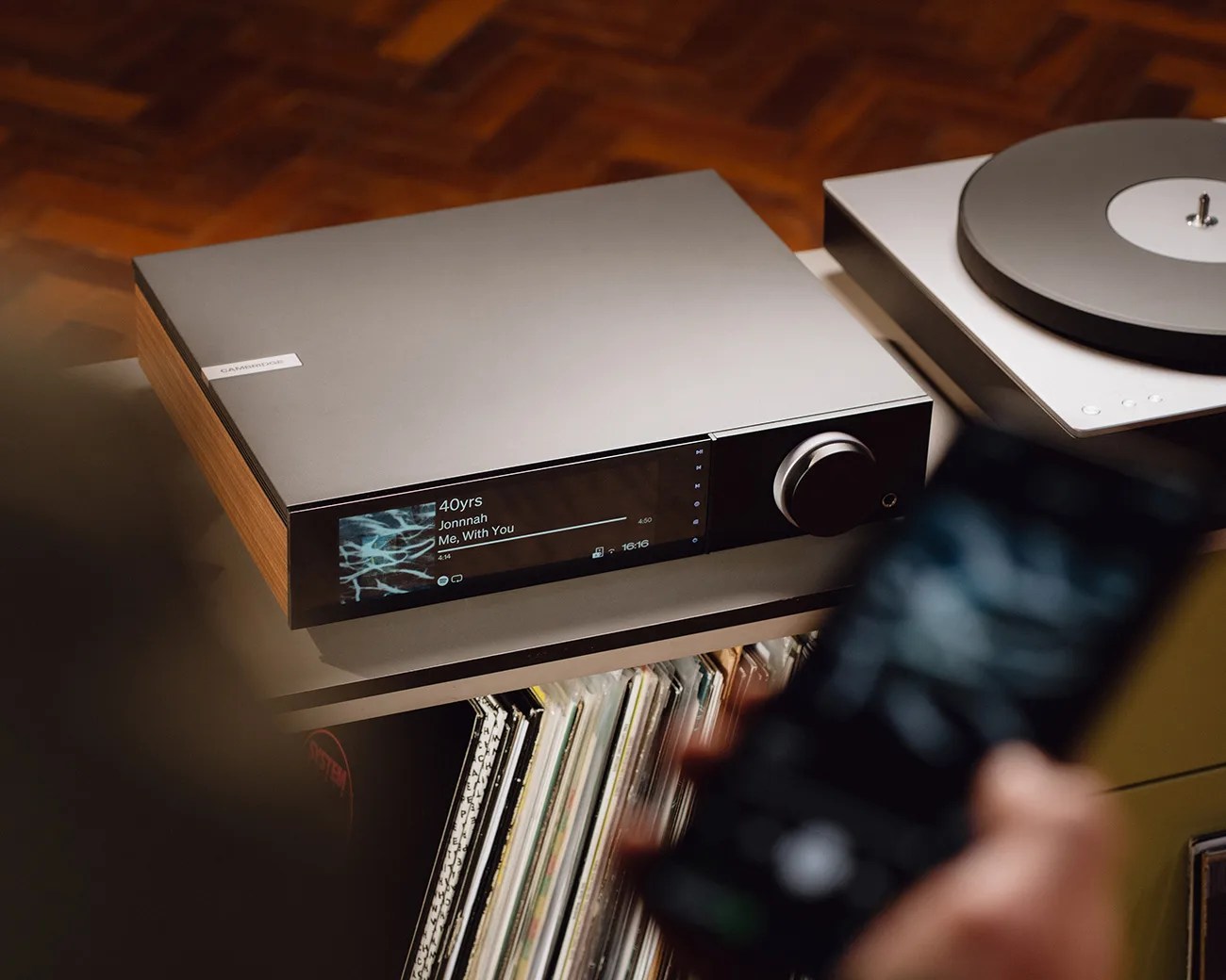 Silver and wood Cambridge audio player with digital display showing song info, next to a white turntable.