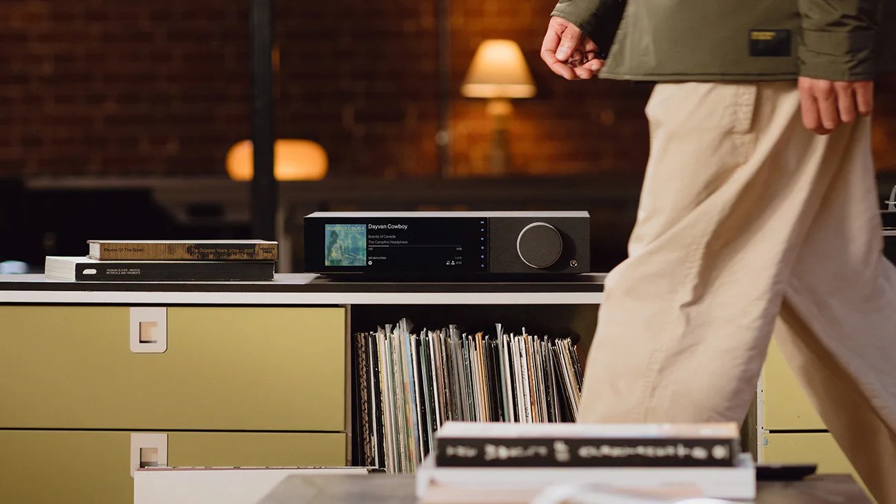 Black audio receiver with a digital display and large volume knob on a white and yellow cabinet with vinyl records and books.