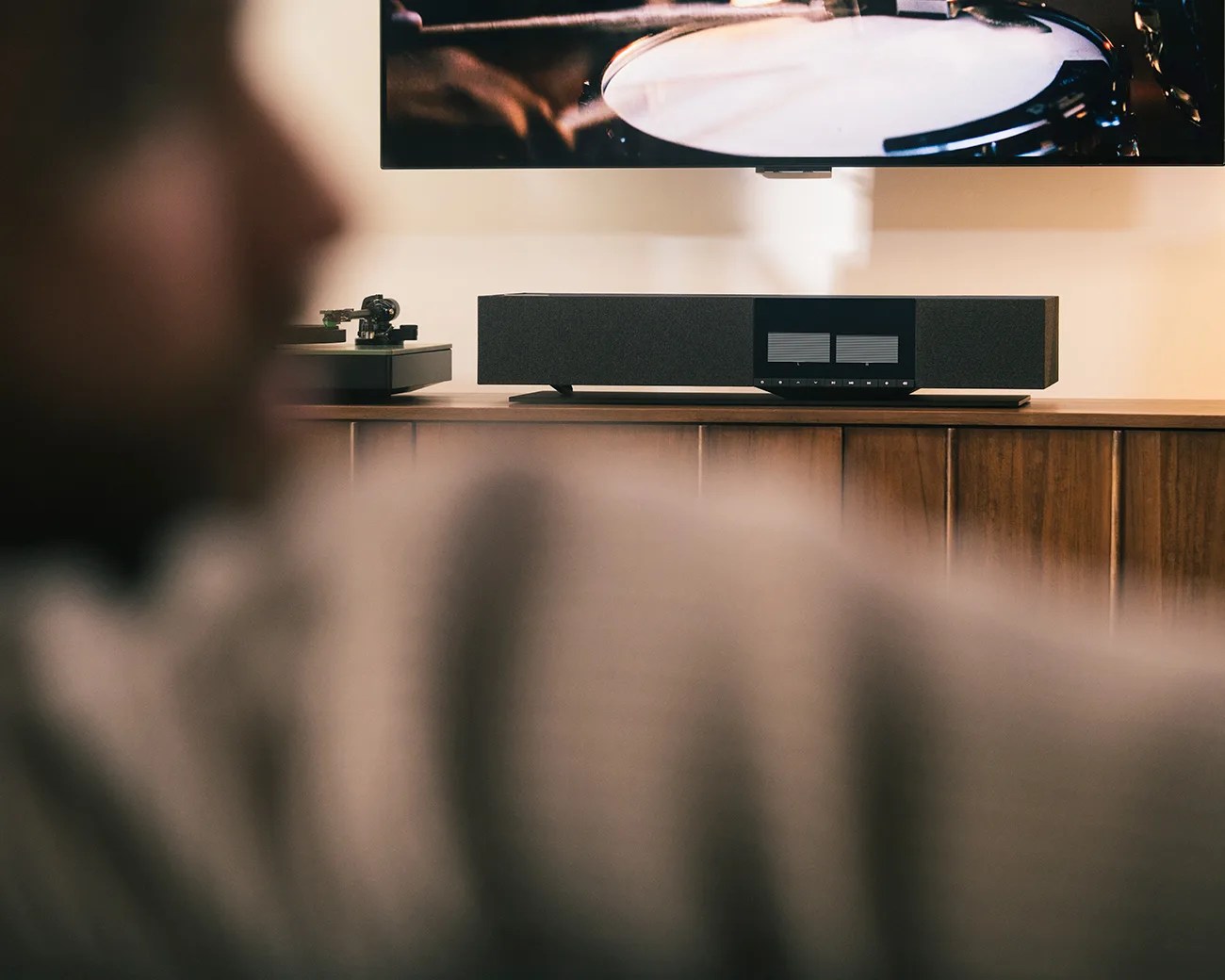 Black rectangular soundbar with control buttons on a wooden cabinet below a wall-mounted TV.