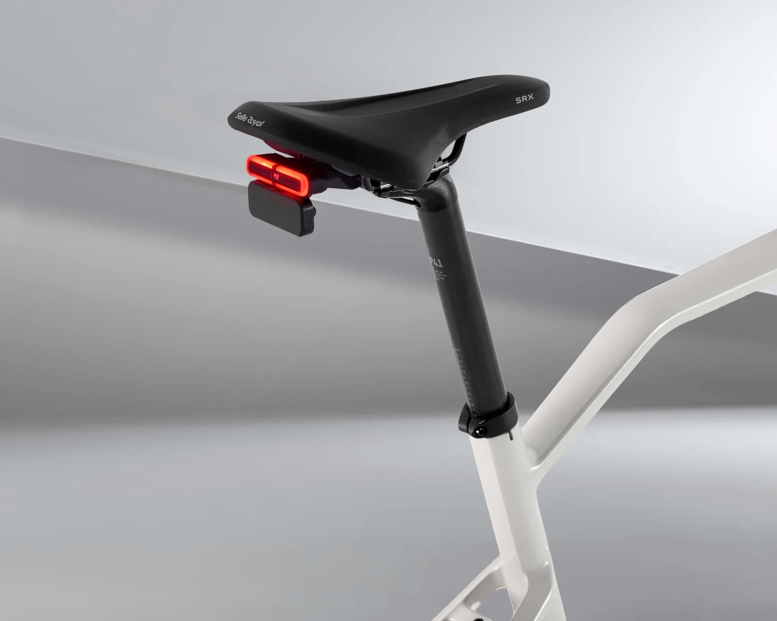 Black Selle Royal SRX bicycle saddle with a red rear light mounted on a white bike frame.