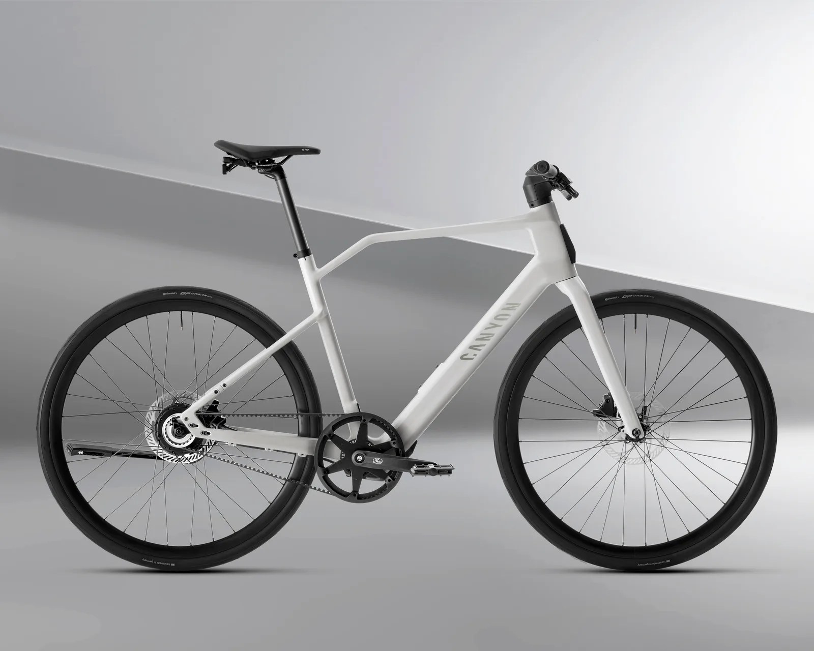 Matte white Canyon electric bike with black saddle, belt drive, and disc brakes on gray background.