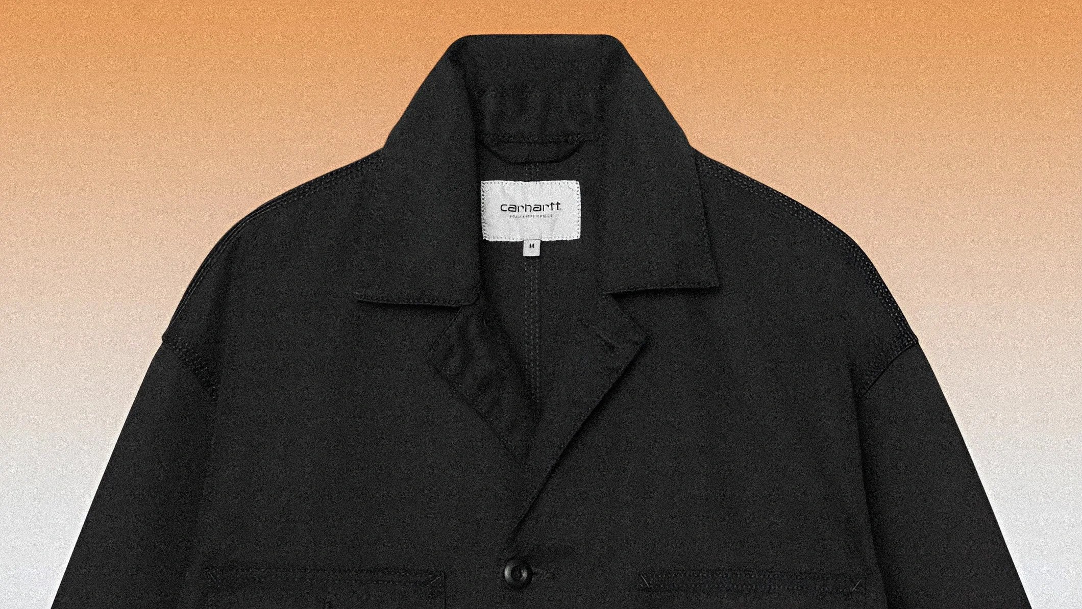 Black Carhartt jacket with collar and button closure on an orange gradient background.