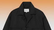 Black Carhartt jacket with collar and button closure on an orange gradient background.