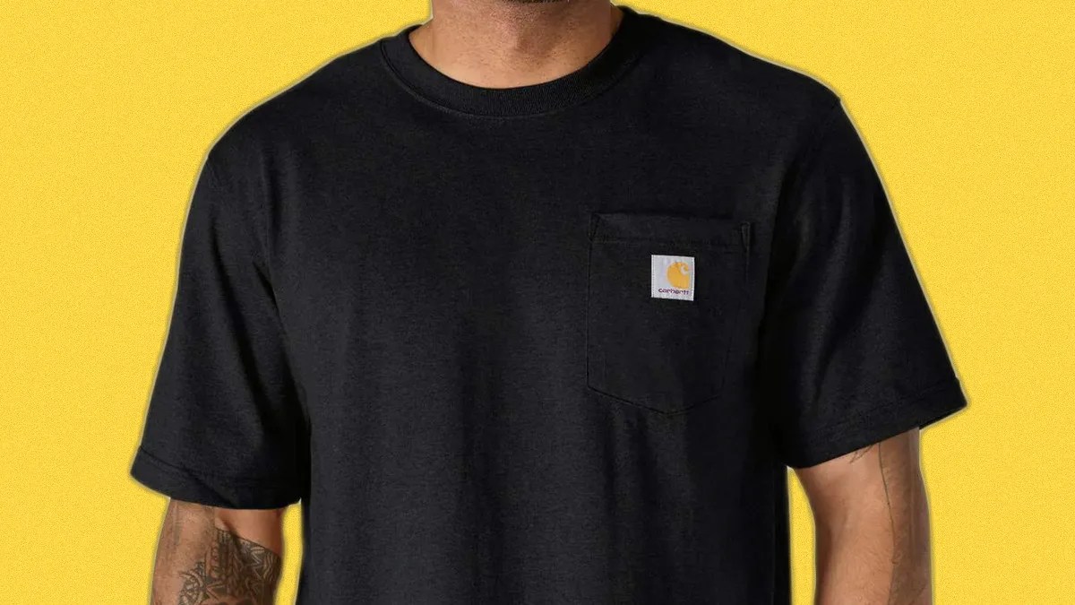 Black Carhartt T-shirt with a chest pocket and logo patch worn by a person against a yellow background.