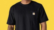 Black Carhartt T-shirt with a chest pocket and logo patch worn by a person against a yellow background.