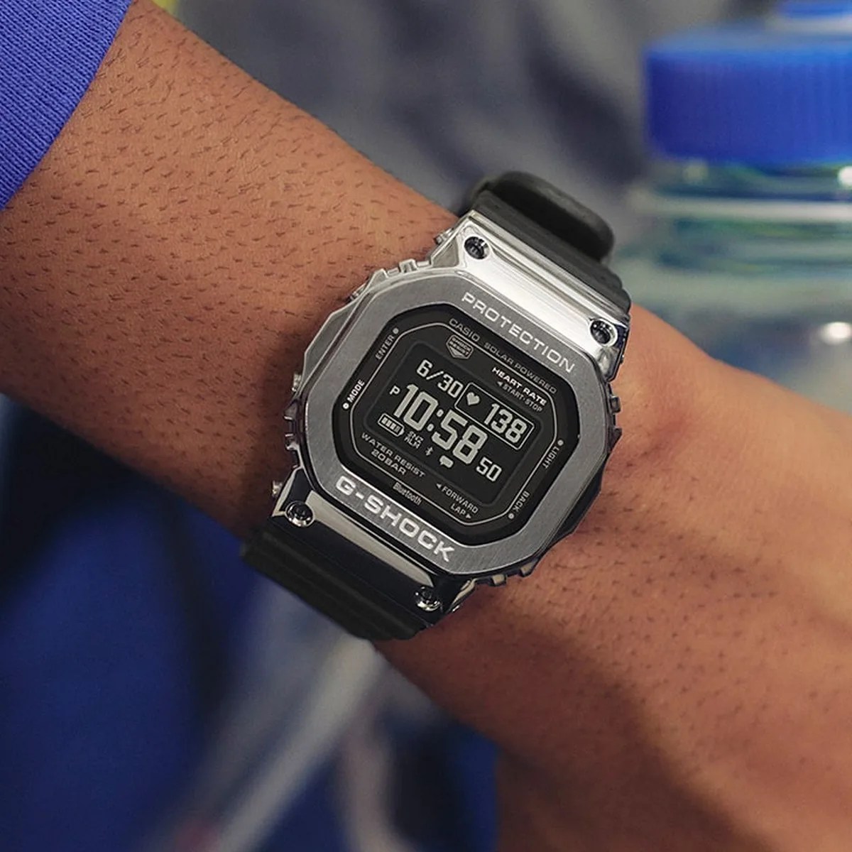 Silver Casio G-Shock digital watch with black resin strap showing time and heart rate on wrist.