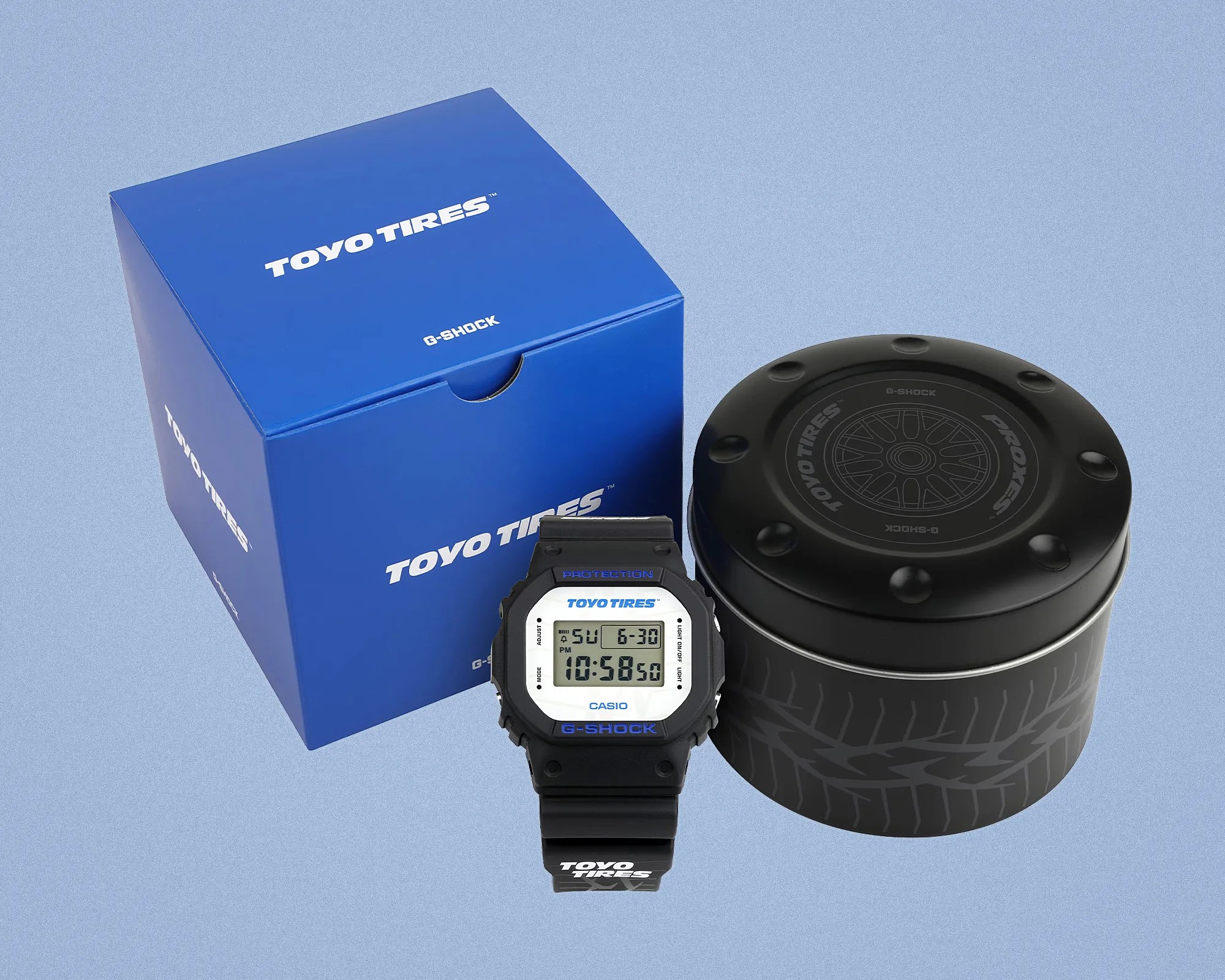 Black Casio G-Shock digital watch with blue "TOYO TIRES" text on the face and strap, next to a blue Toyo Tires box and black cylindrical container.