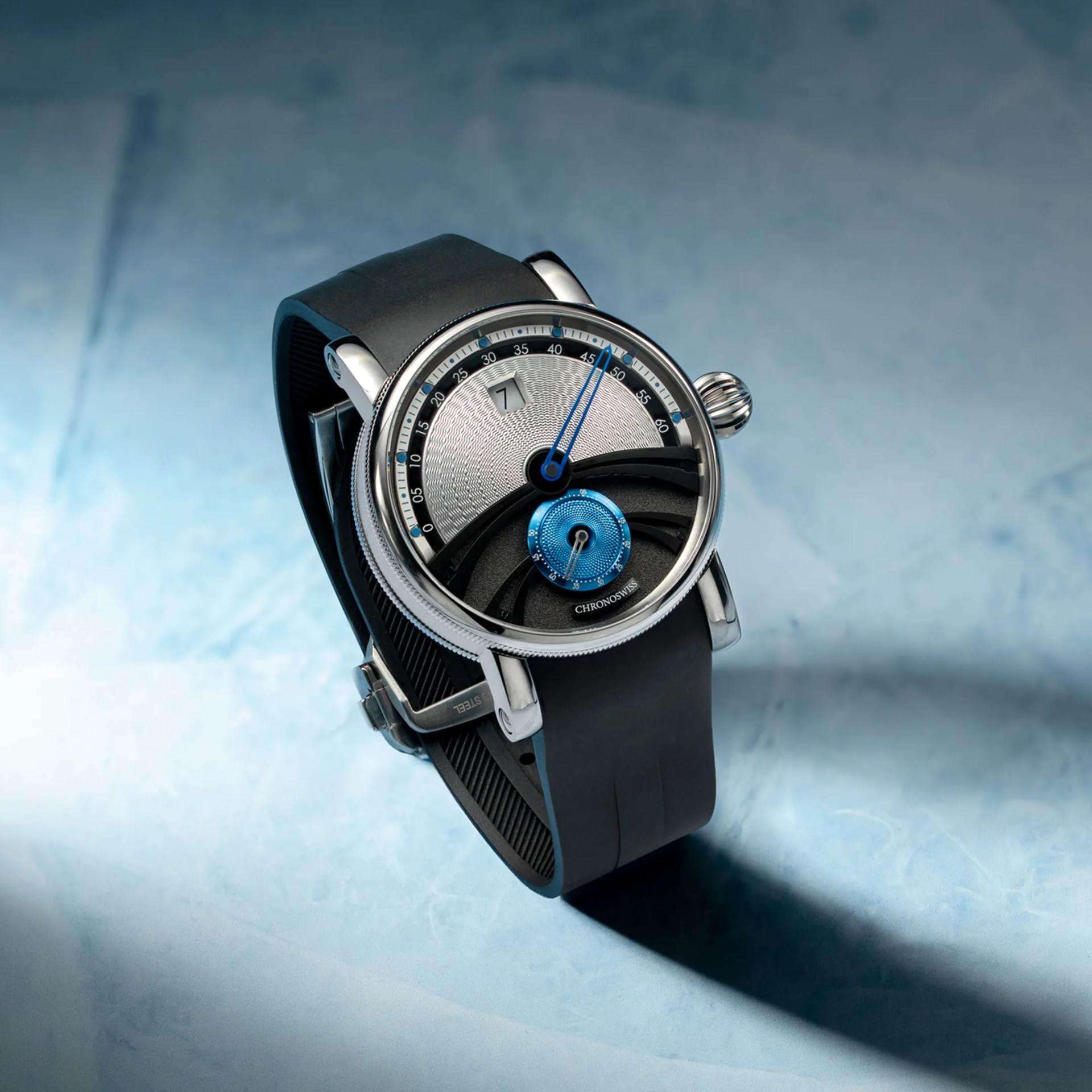 Silver and black Chronoswiss wristwatch with blue accents and black rubber strap on a blue surface.