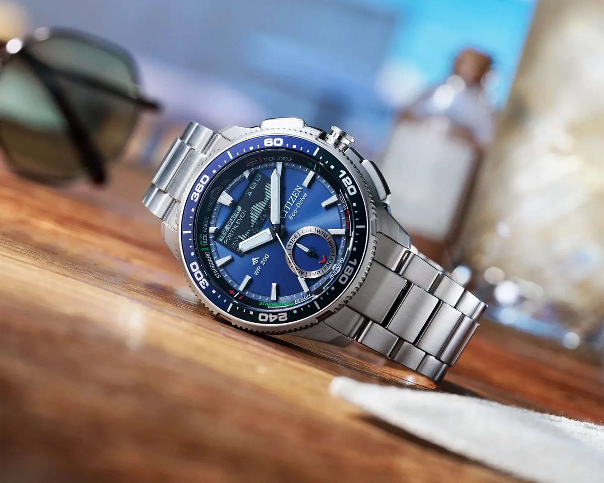 Silver metal Citizen Eco-Drive wristwatch with blue dial and multiple subdials on a wooden surface.