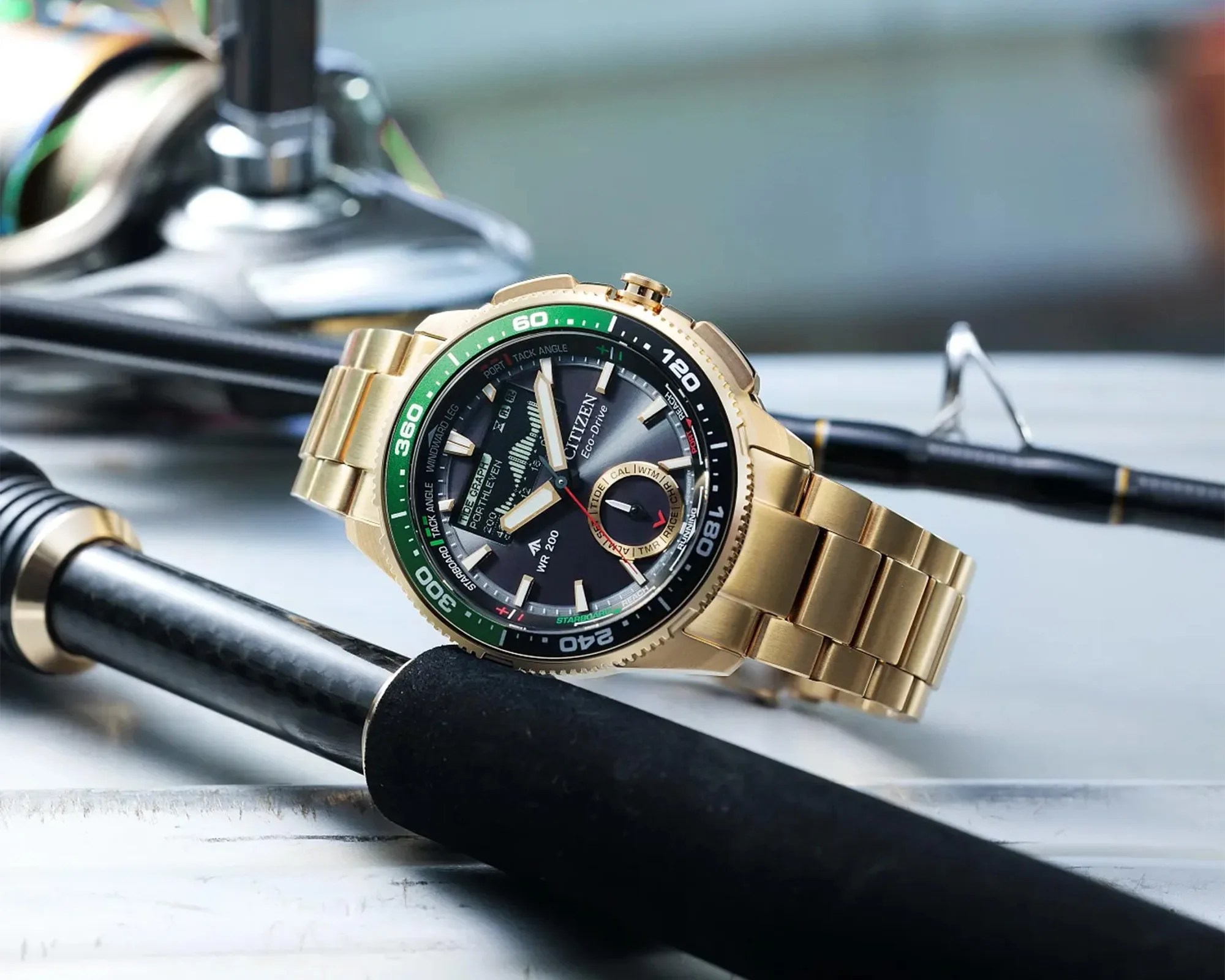 Gold Citizen Eco-Drive wristwatch with green and black bezel resting on black fishing rods.