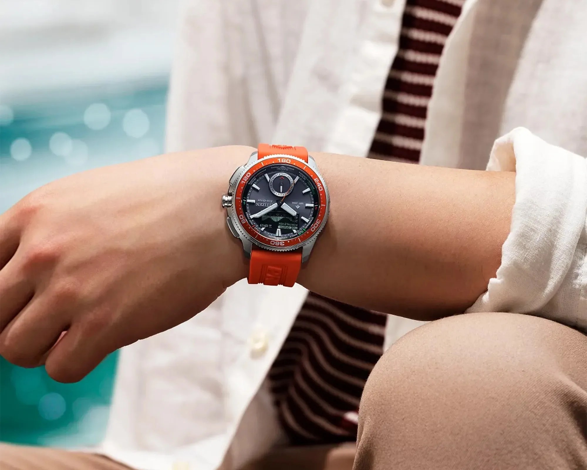 Wristwatch with orange rubber strap and black dial worn on a person's wrist.