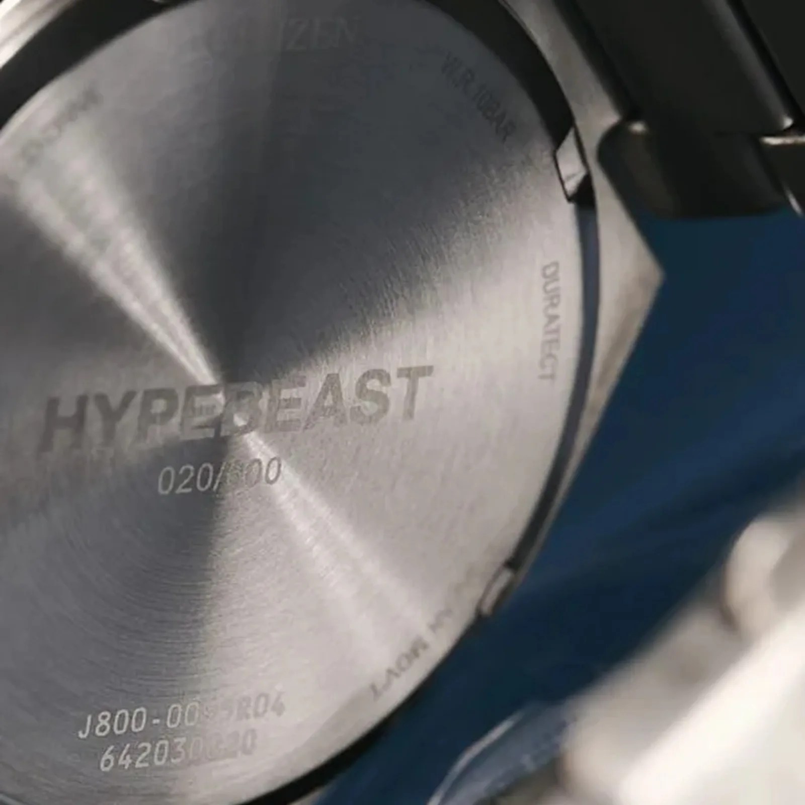 Close-up of a metallic watch case back with engraved text "HYPEBEAST" and serial numbers.