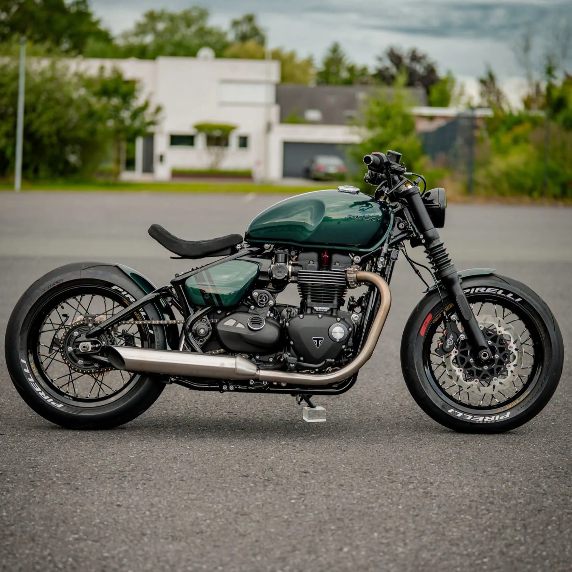 Green custom cafe racer motorcycle with black frame and Pirelli tires parked on asphalt.